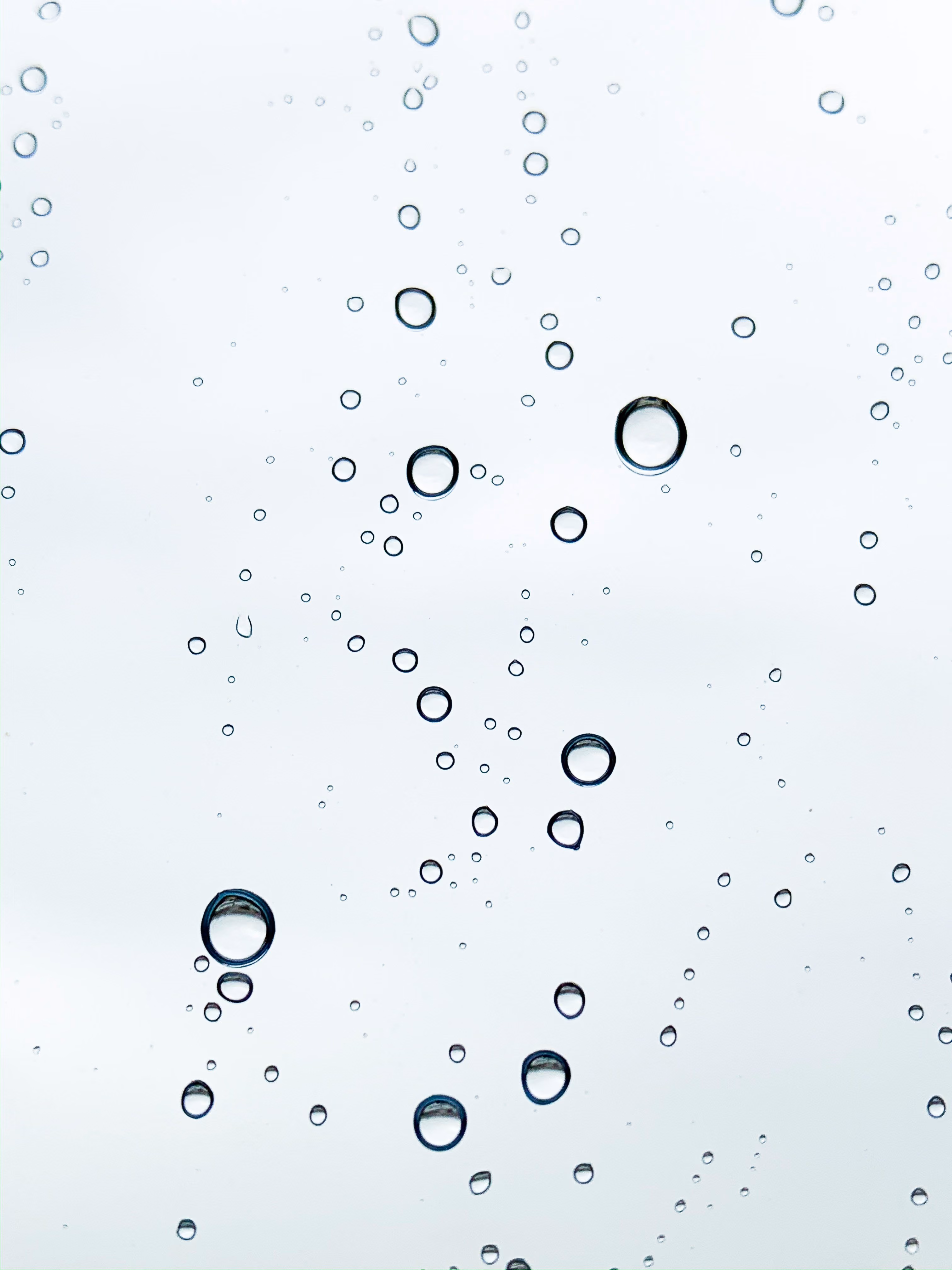 Close-up of multiple water droplets on a clear surface against a soft light background.