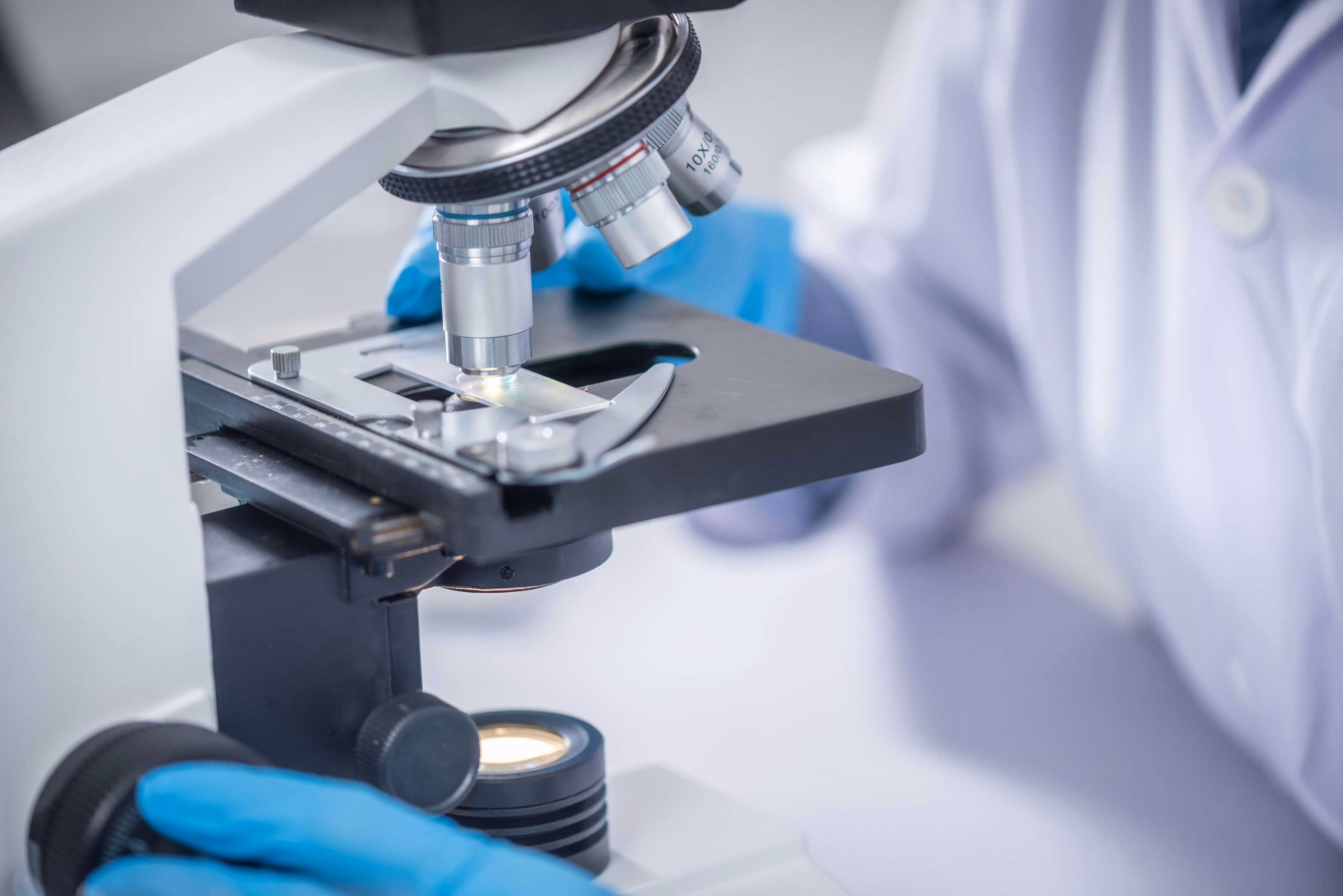 Scientist adjusting a microscope with blue gloves and a lab coat in a laboratory setting.