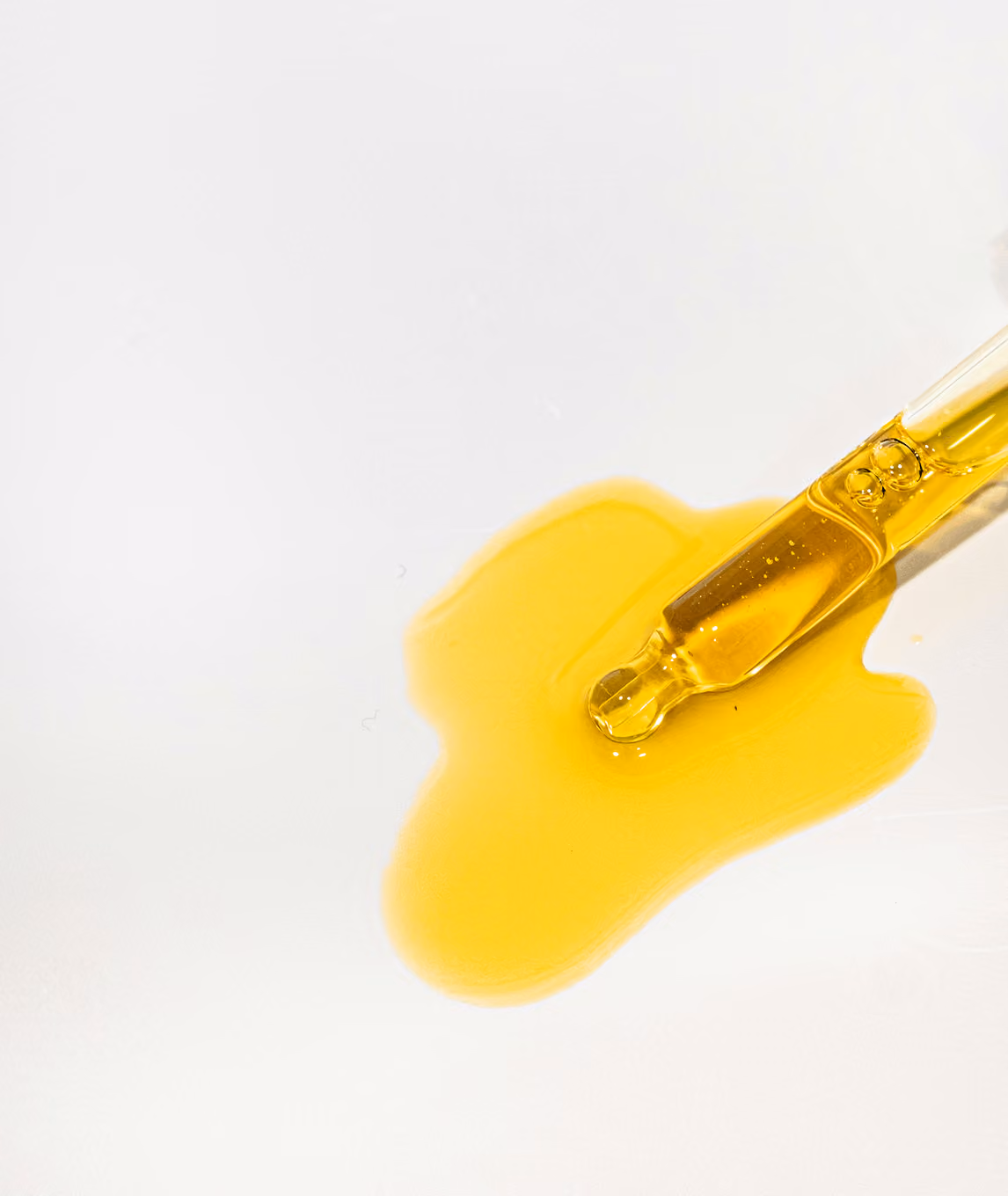 Close-up of a dropper with golden-yellow oil on a white surface.