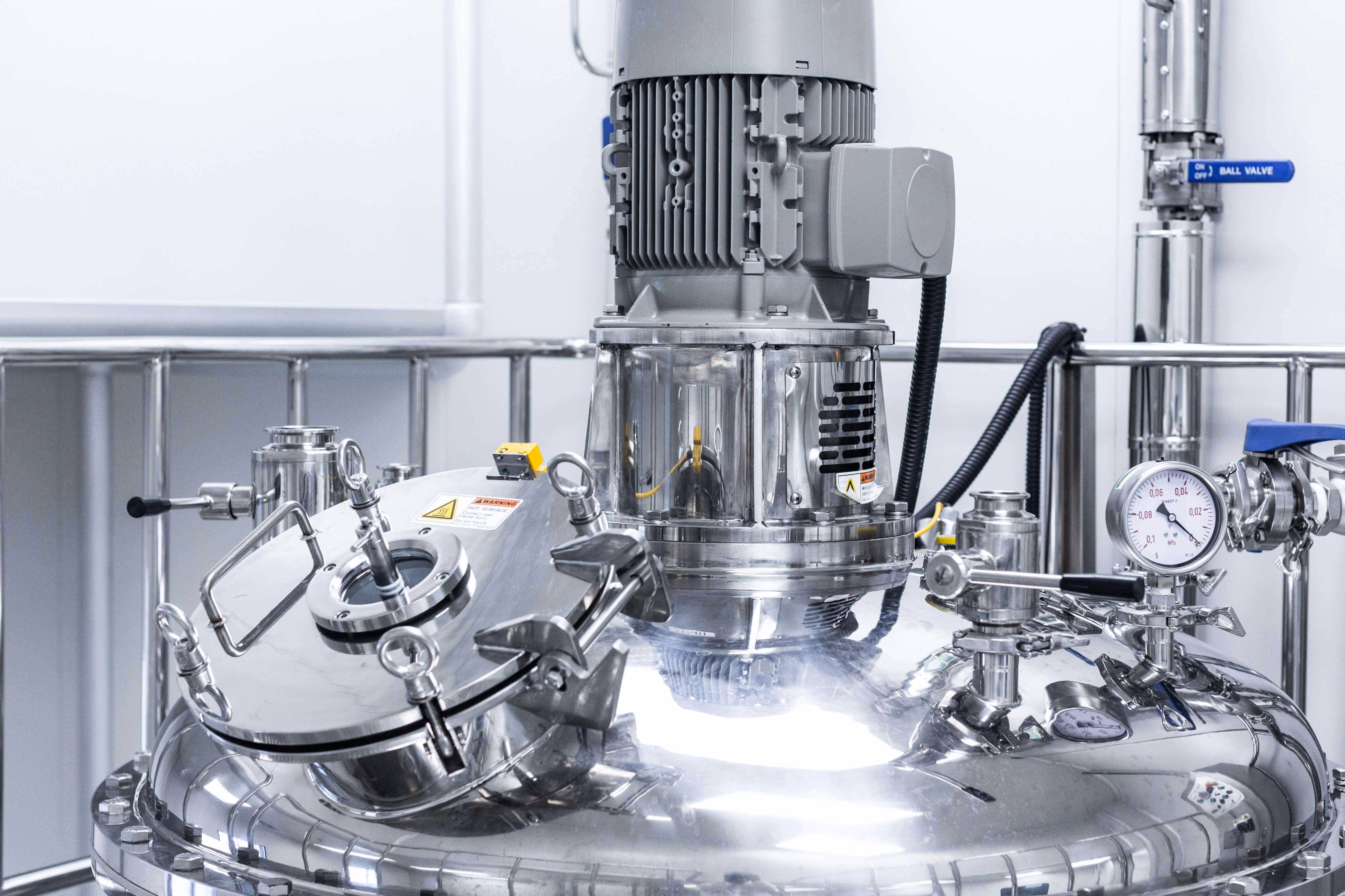 Close-up of stainless steel industrial mixing tank with pressure gauge and motor in a clean facility.