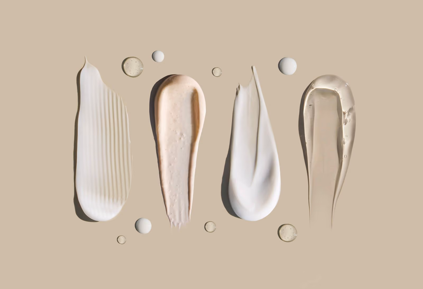 Four different textured cosmetic cream and gel swatches on a beige background.