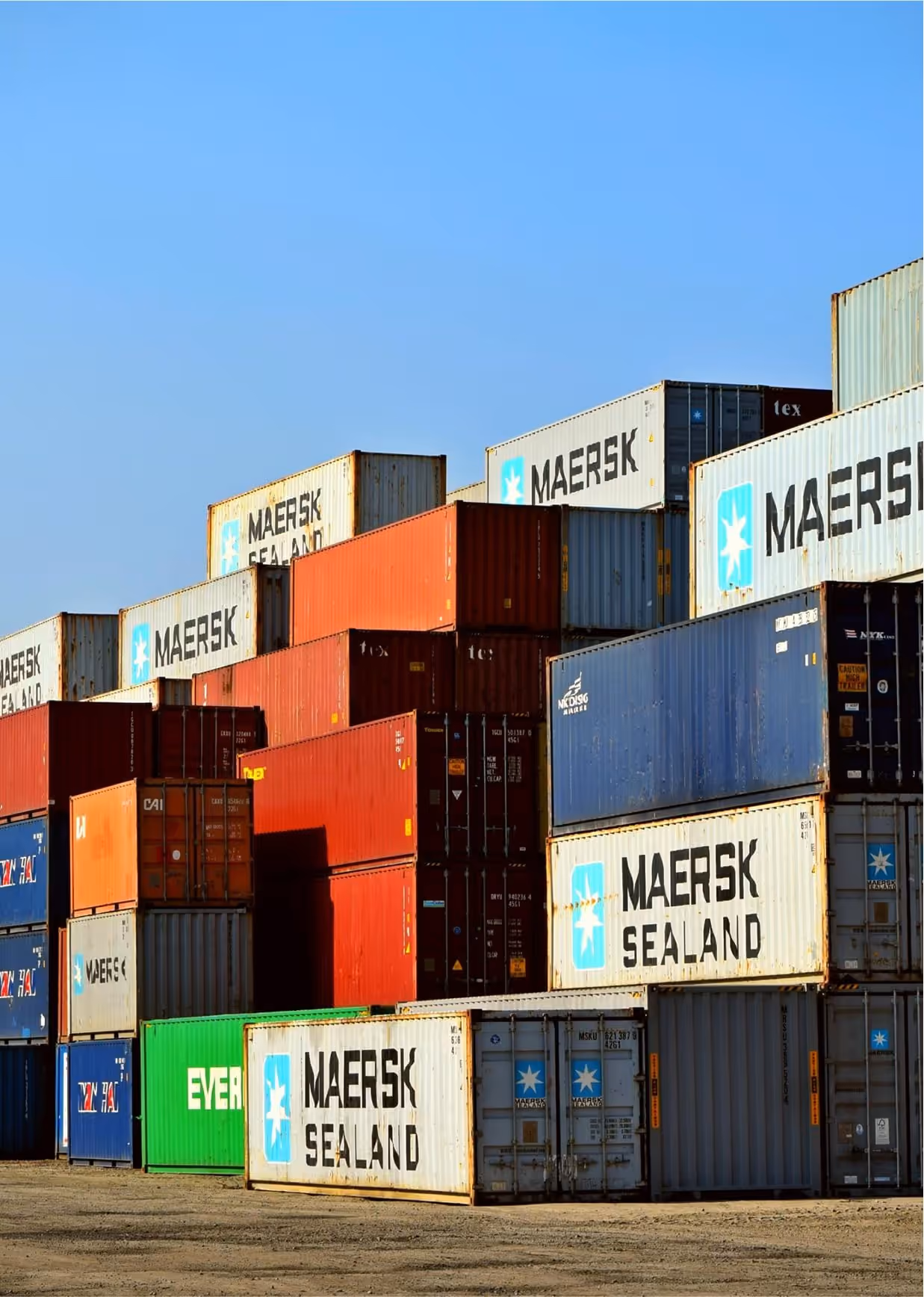 Stack of multicolored shipping containers, many branded with Maersk Sealand, under clear blue sky.