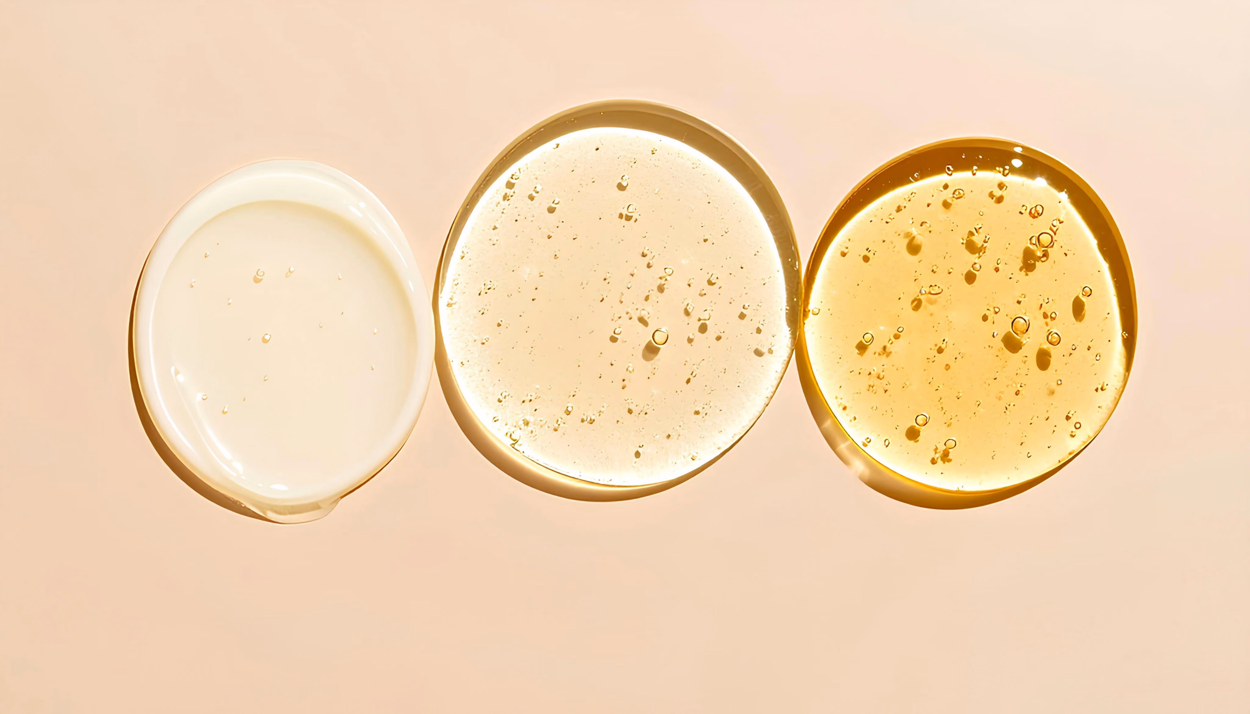 Three circular serum drops in varying yellow shades with bubbles on a beige surface.