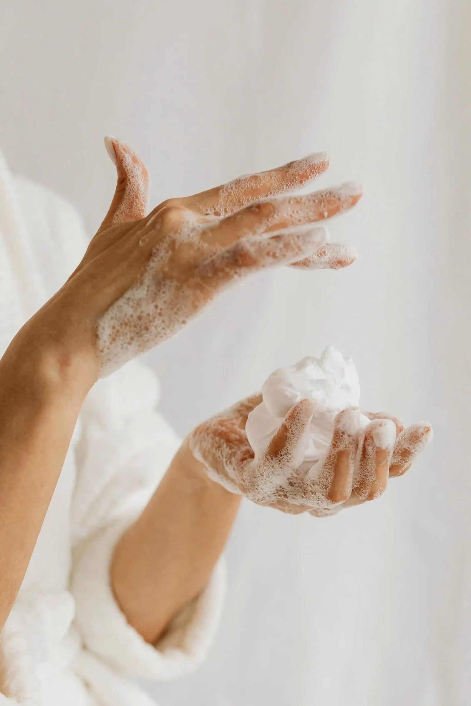 Hands covered in soap lather, one holding foam, against a light background.
