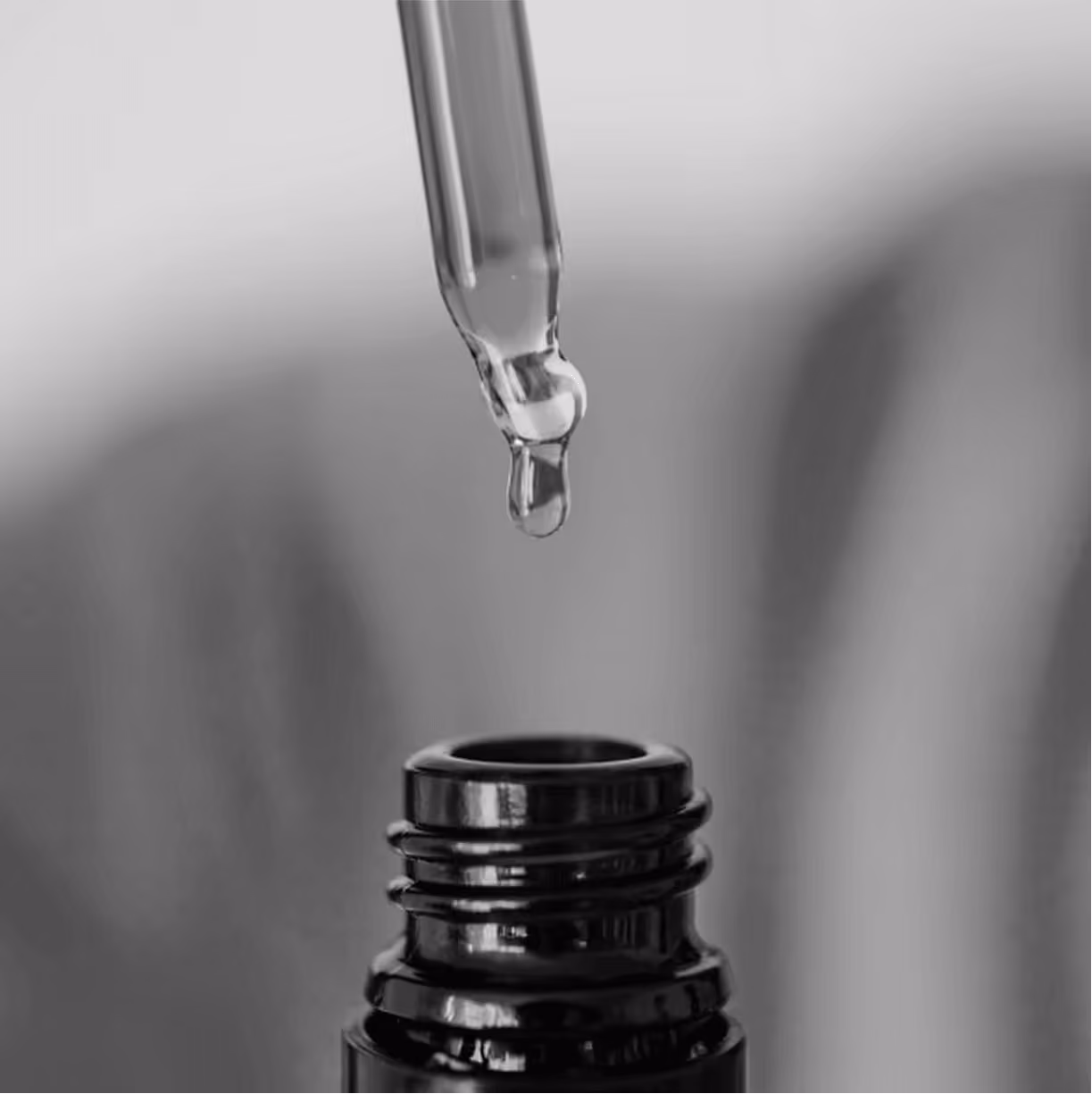 Dropper releasing a drop of liquid into a small dark bottle.