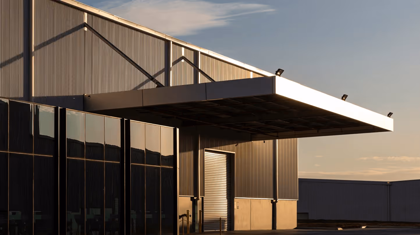 Exterior of a modern warehouse with large glass windows and a closed loading dock door at sunset.