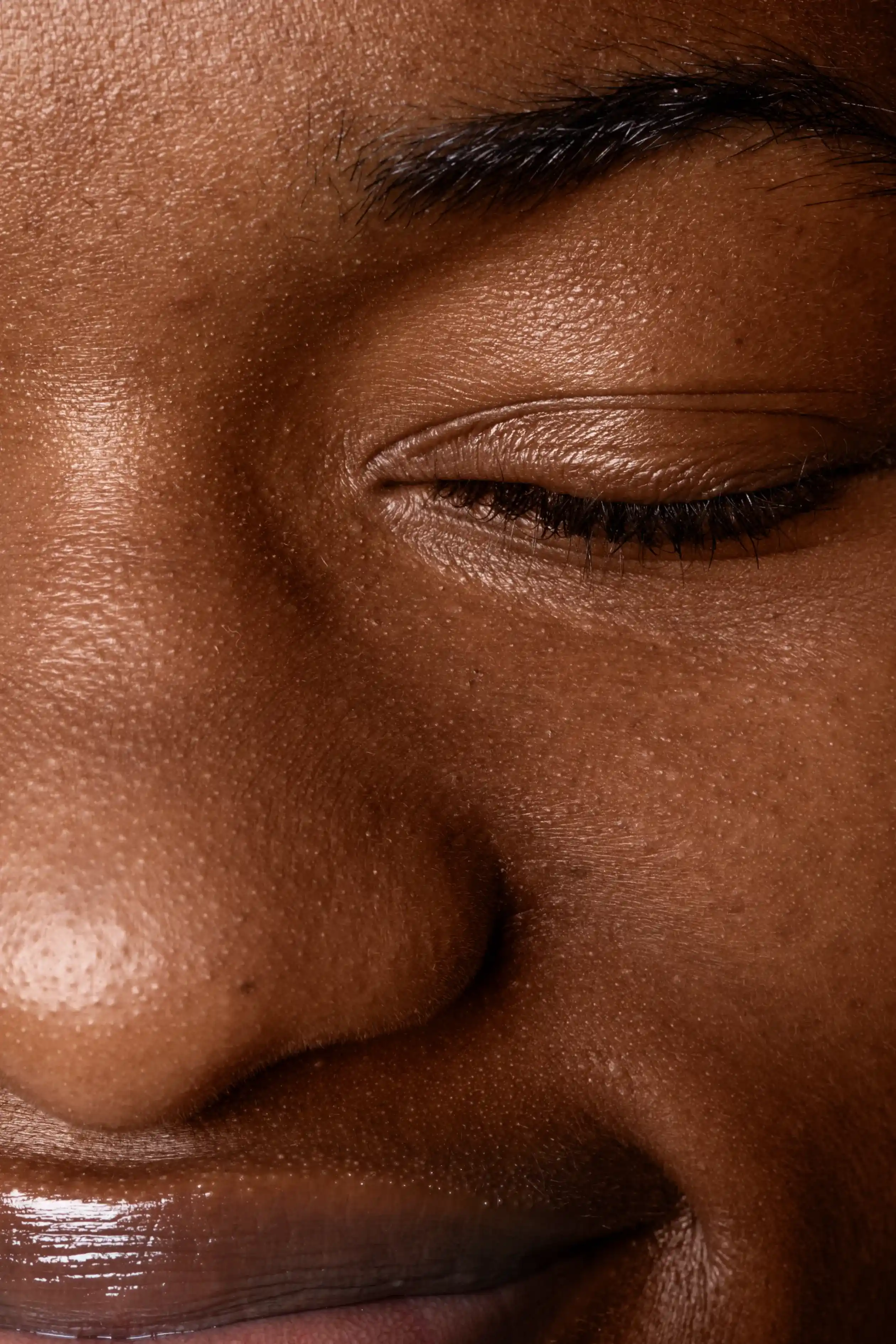 Close-up of a person's face showing closed eye, eyebrow, nose, and part of the lips with visible skin texture and pores.