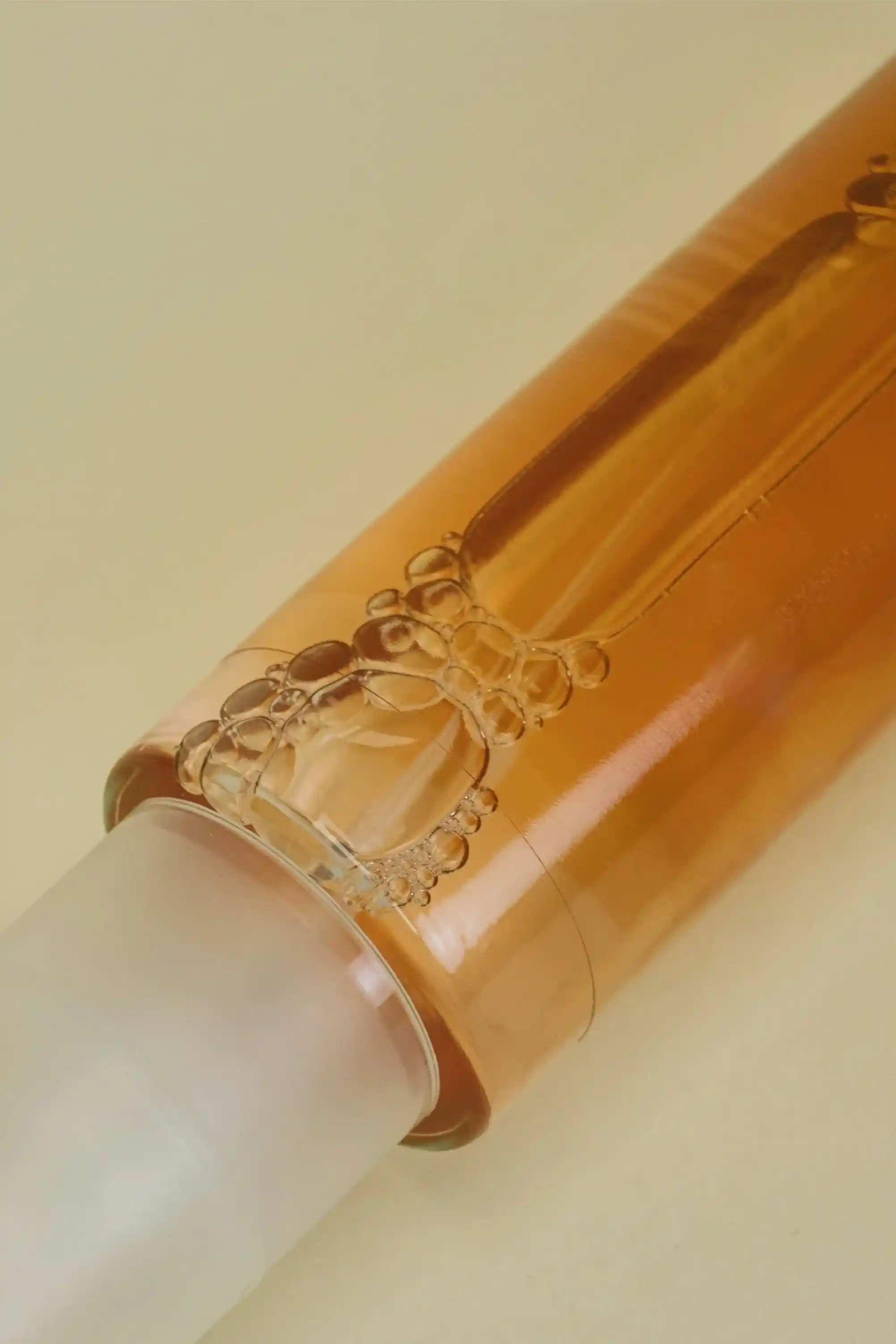 Close-up of a transparent bottle with amber liquid and bubbles near the cap on a light background.