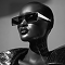 Futuristic portrait of a person with shiny skin wearing black sunglasses and a metallic jacket.