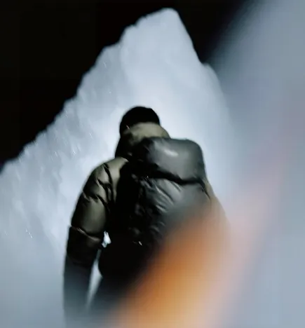 Person facing a large illuminated ice or snow structure in a dark setting.