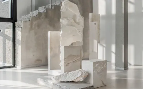 Abstract white stone sculptures and slabs arranged on a light floor with shadows and large windows.