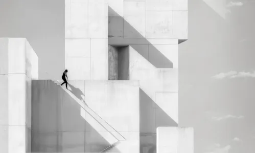 Silhouetted person walking down large white geometric concrete stairs with sharp shadows.