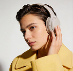 Person wearing beige headphones and a yellow coat holding one side of the headphones.