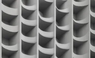 Close-up of a geometric pattern of curved, vertical concrete panels in soft gray tones.