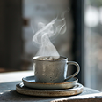 Mug with coffee emitting steam on stacked ceramic plates on a wooden table.