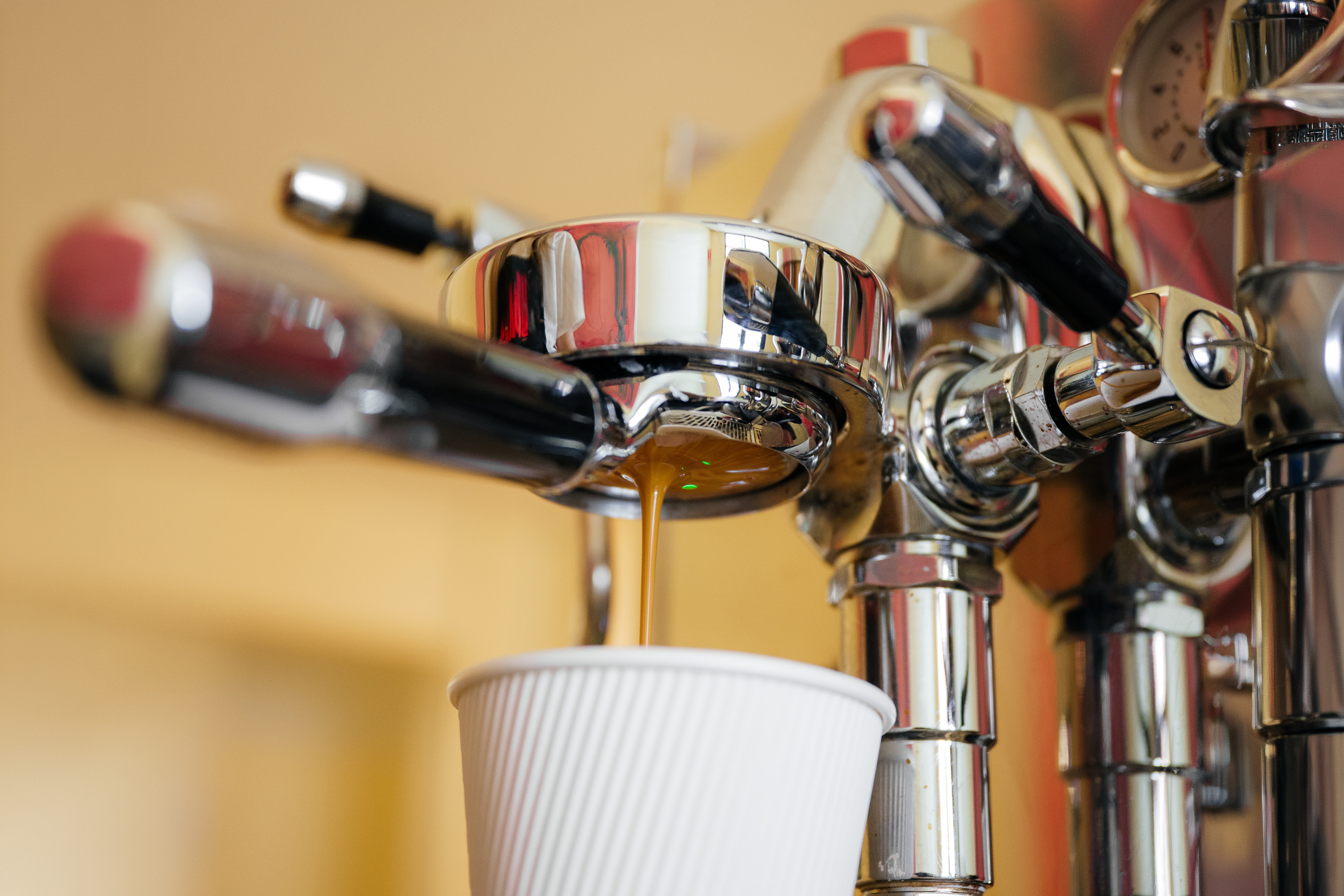 Espresso machine dispensing coffee into a white paper cup.