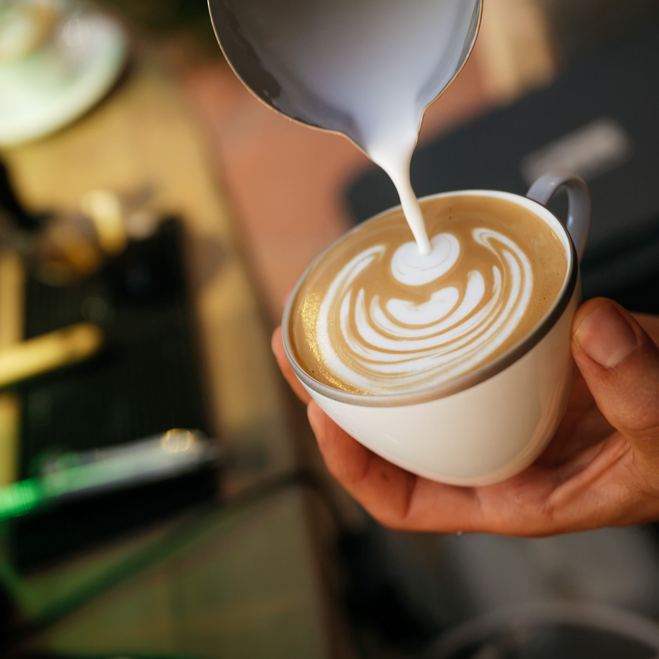 Close-up of hand pouring steamed milk to create latte art in a white coffee cup.