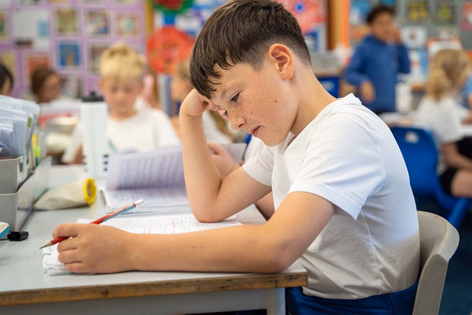 Pupil resting his head on his hand while writing at his classroom desk.