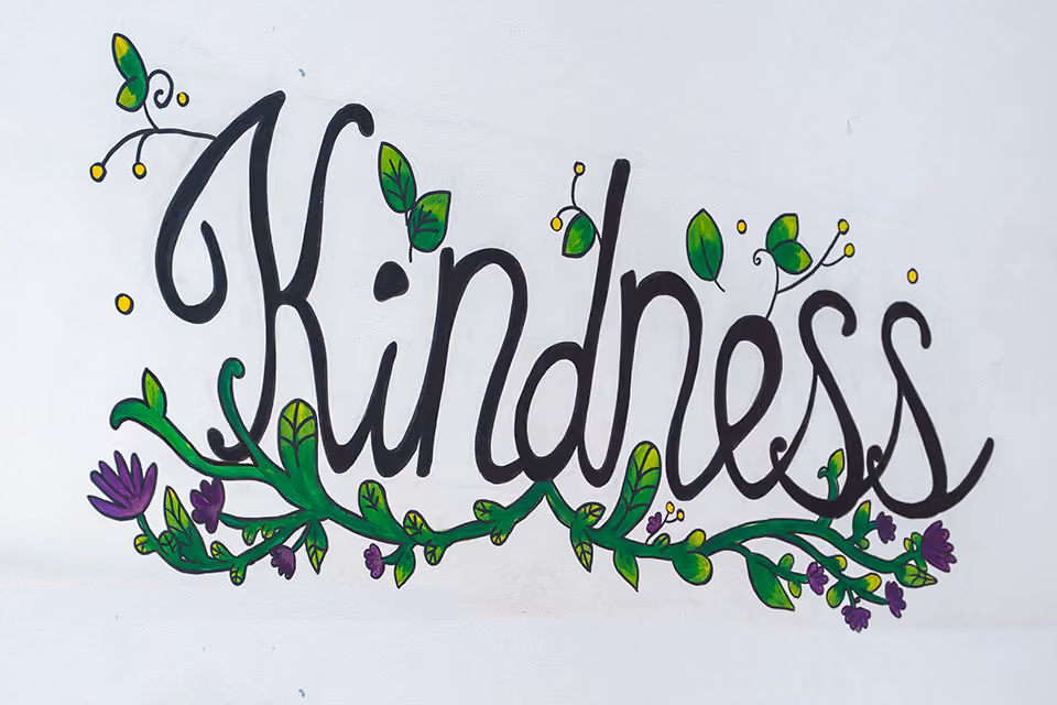 Hand-painted wall lettering reading ‘Kindness’, decorated with green leaves and purple flowers.