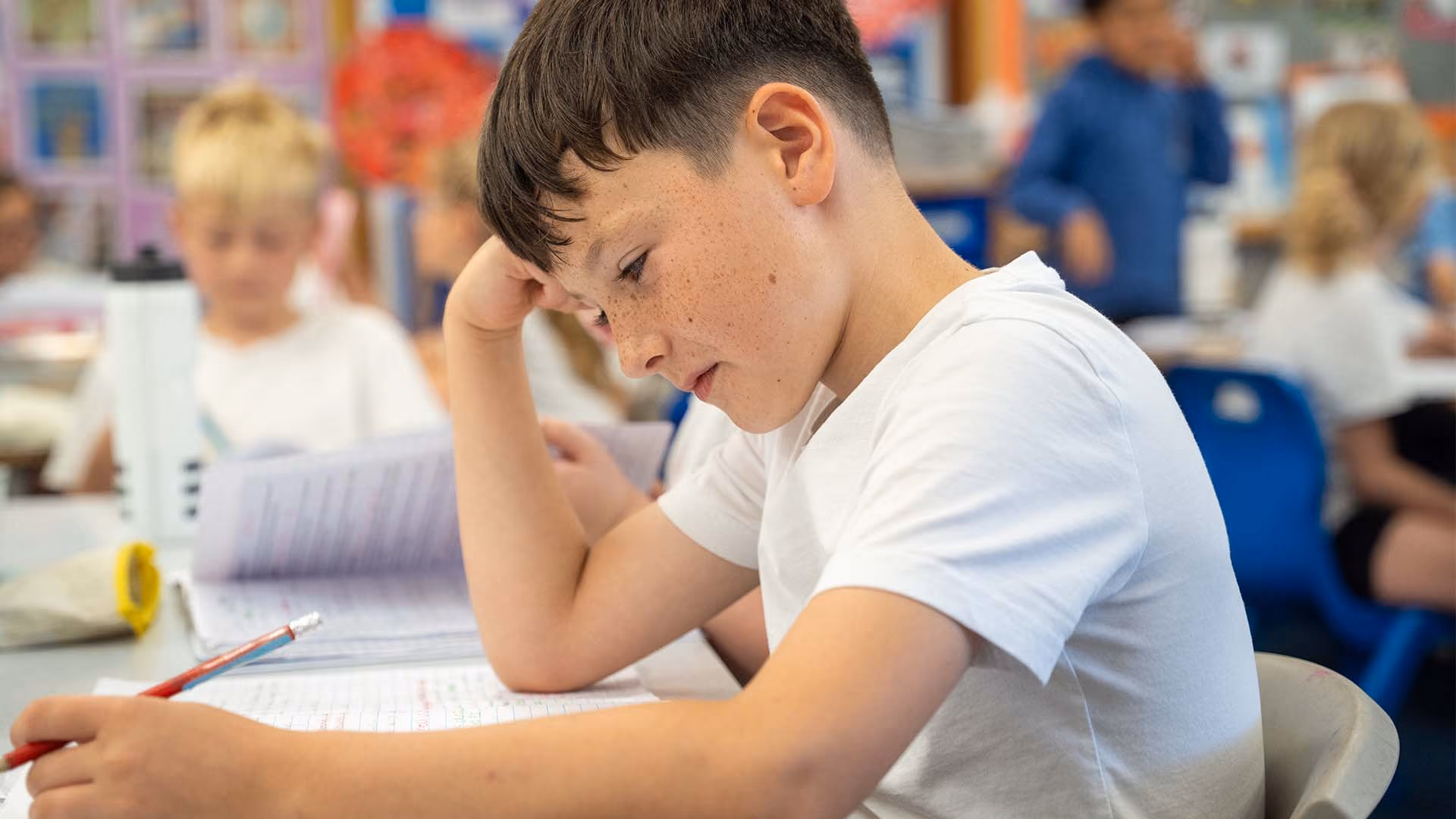 Pupil resting his head on his hand while writing at his classroom desk.