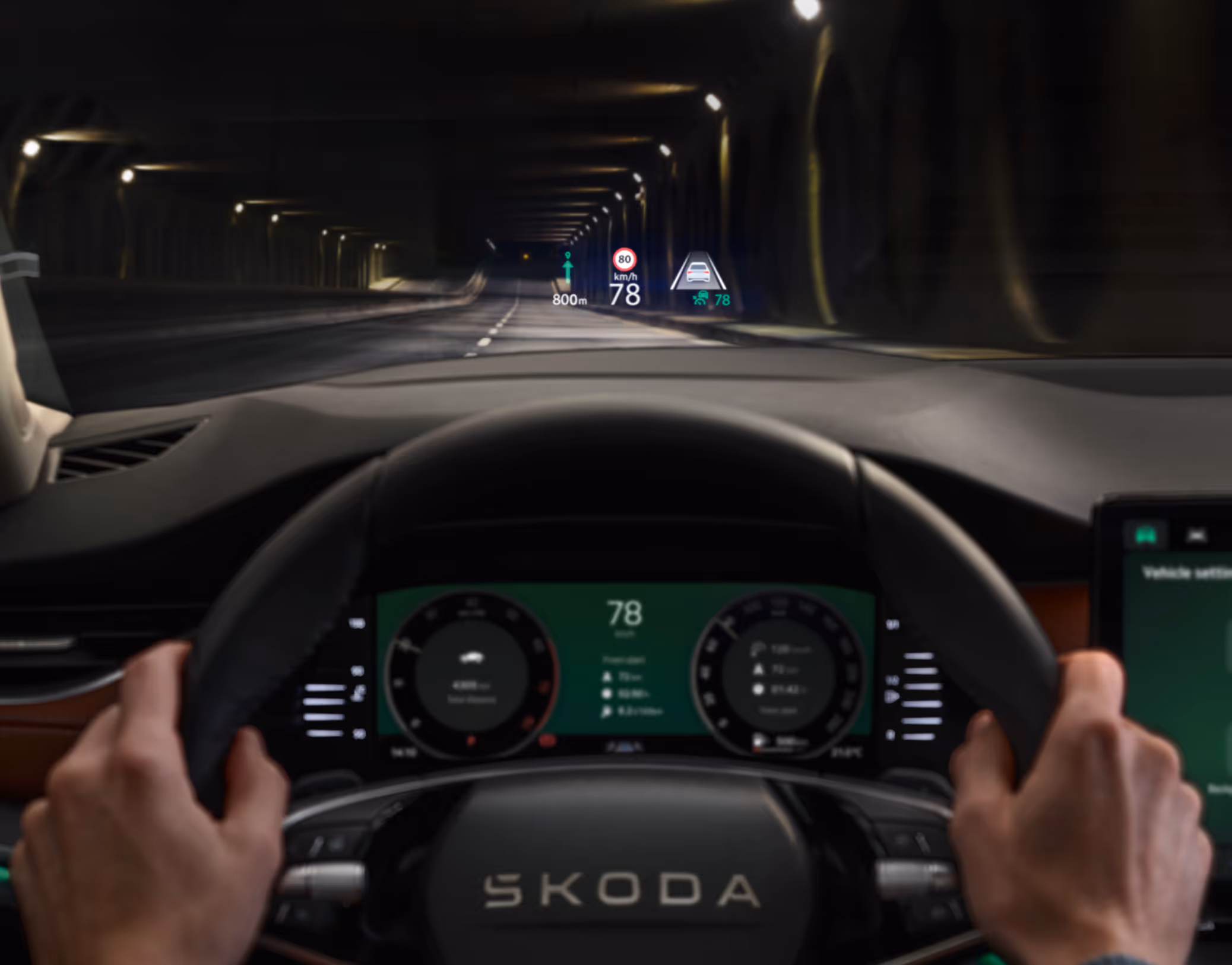 Das Bild zeigt die Fahrerperspektive im Škoda Octavia 30 Jahre während einer Fahrt durch einen dunklen Tunnel. Im Fokus steht das Head-up Display, das Informationen wie die aktuelle Geschwindigkeit und Navigationshinweise direkt in das Sichtfeld auf die Frontscheibe projiziert. Darunter ist das digitale Kombiinstrument hinter dem Zweispeichen-Multifunktionslenkrad zu erkennen, das die aktuellen Fahrdaten anzeigt.