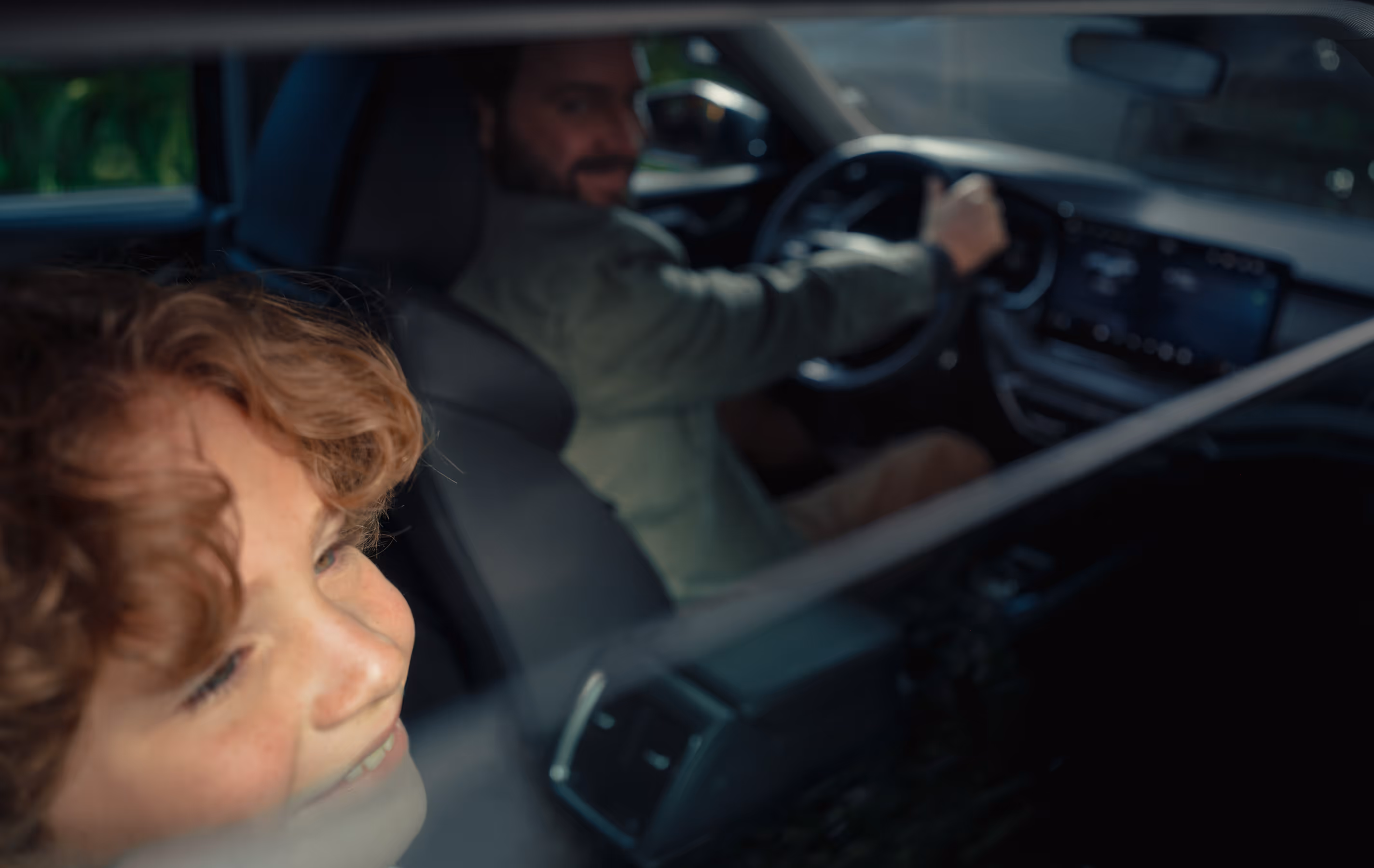 Eine Nahaufnahme durch das geöffnete Seitenfenster in den Innenraum des Škoda Octavia 30 Jahre zeigt im Vordergrund das lachende Gesicht eines Jungen auf der Rückbank. Im unscharfen Hintergrund ist der Fahrer am Steuer sowie ein Teil des Armaturenbretts mit dem beleuchteten Infotainment-Display zu erkennen. Das Bild vermittelt einen Eindruck der geräumigen Kabine und der Interieur-Ausstattung während einer Fahrt.