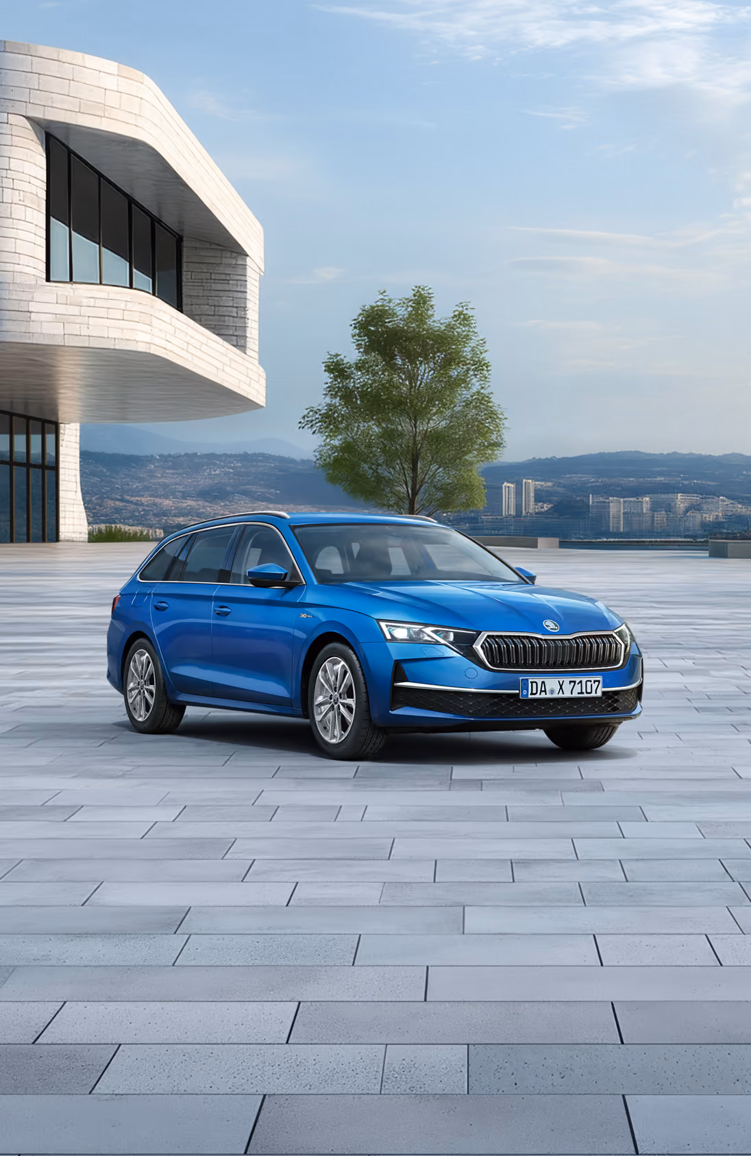Das Bild zeigt das Sondermodell Škoda Octavia Combi 30 Jahre in der Farbe Race-Blau Metallic aus der vorderen linken schrägen Perspektive auf einem weitläufigen, gepflasterten Platz vor einer Stadtkulisse. Zu sehen sind Exterieur-Details wie die silbernen Leichtmetallfelgen, der Kühlergrill mit Chromrahmen sowie die schwarze Dachreling. Am unteren linken Bildrand hebt ein hellgrüner Störer einen Preisvorteil sowie die inkludierte 5-Jahres-Garantie hervor.