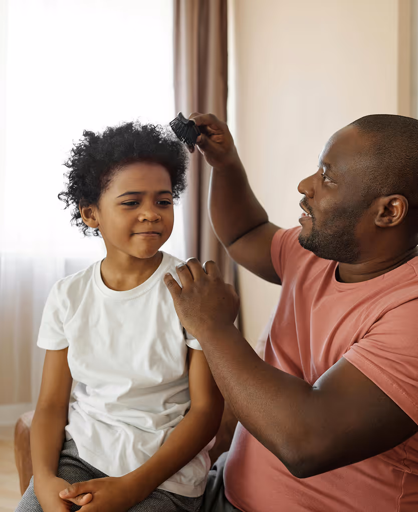 Man combing a young boy's curly hair while the boy sits with hands clasped.