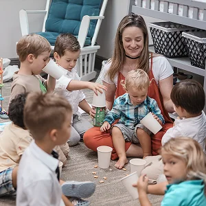 Woman and children sitting on floor indoors playing with paper cups and smiling.