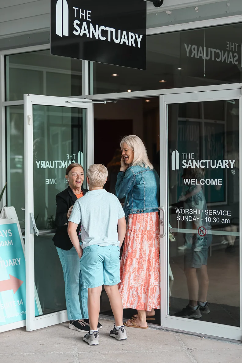 Three people greeting each other at the open doors of The Sanctuary church entrance.