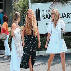 Three women walking and talking outside a building with a Sanctuary sign in the background.