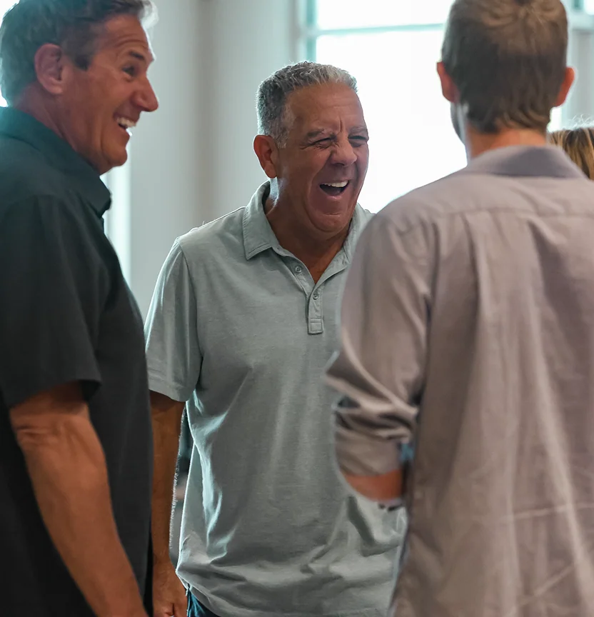 Group of men laughing together indoors near a window with natural light.