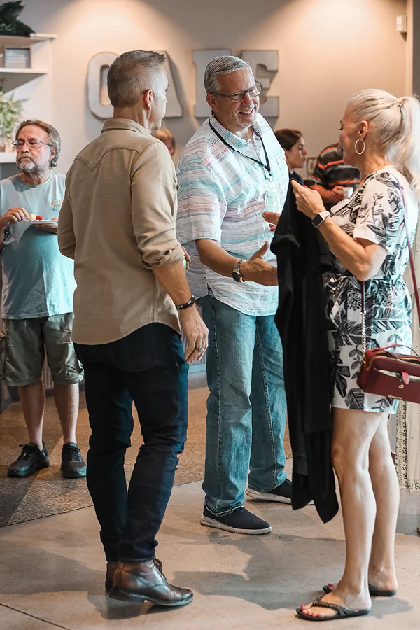 Three adults chatting and smiling at a casual indoor social event, two men and one woman.