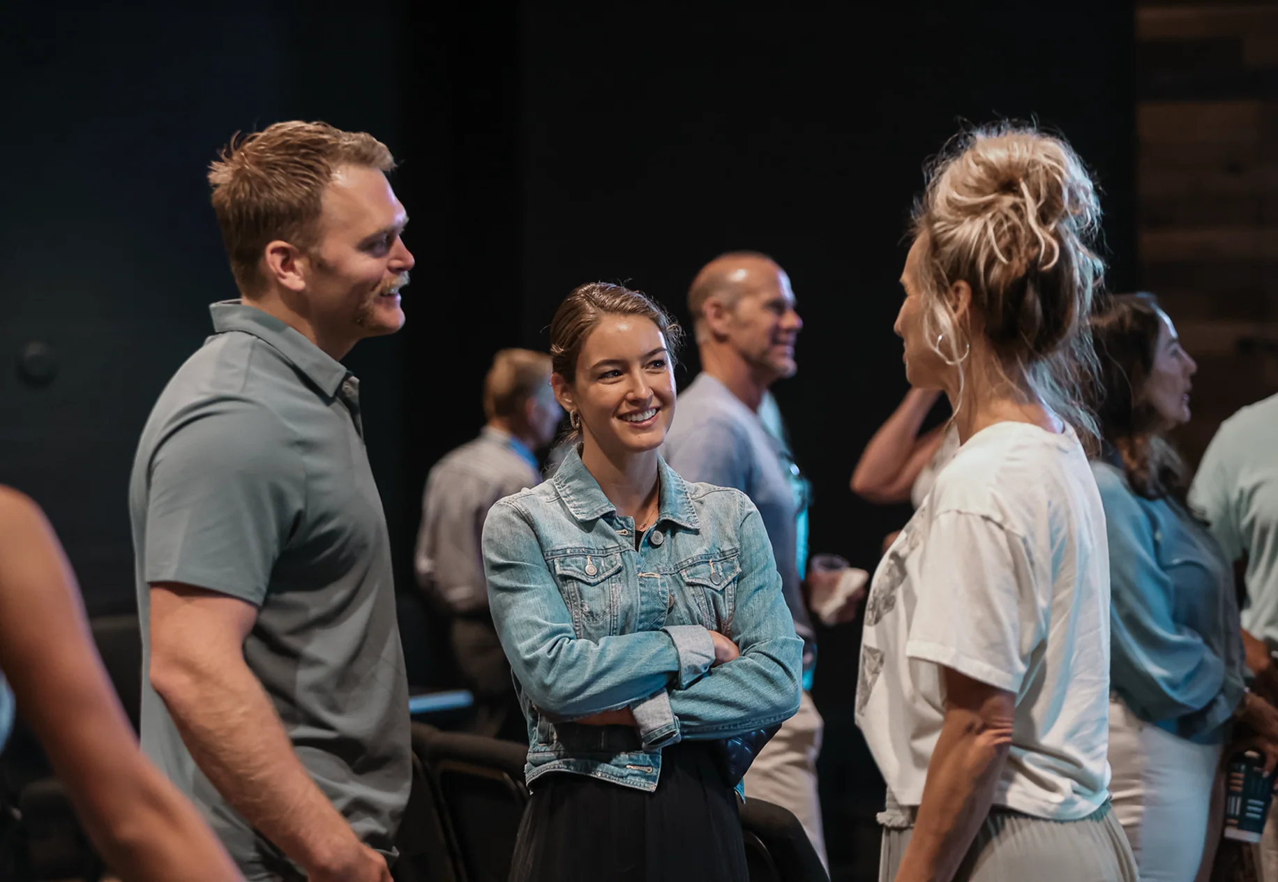 Group of people smiling and chatting indoors in casual clothing, engaging in friendly conversation.