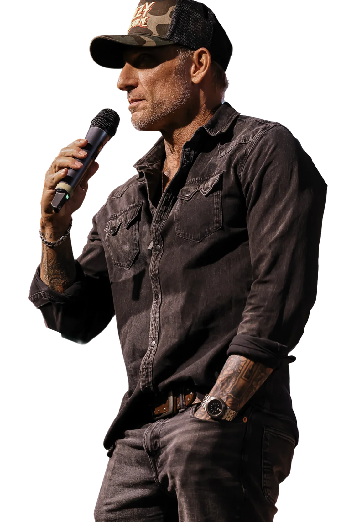 Man in casual dark shirt and camo cap speaking into microphone with one hand in pocket.