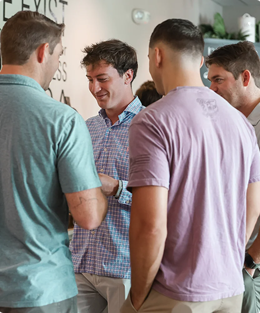 Four men standing close together engaged in conversation in a casual indoor setting.