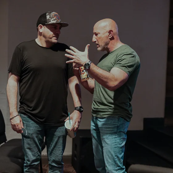 Two men in casual clothes having an engaged conversation indoors, one gesturing with his hands.