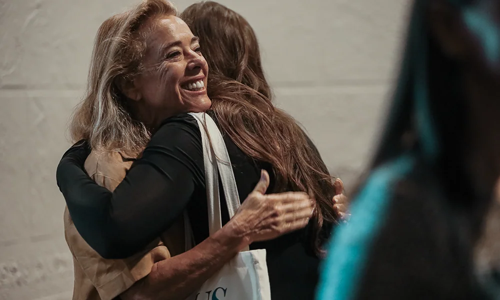 Two women sharing a warm hug, one smiling happily with beige and black clothes.