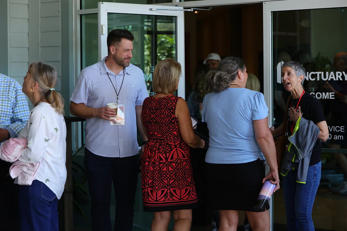 People gathered and conversing near glass entrance doors of a building during daytime.