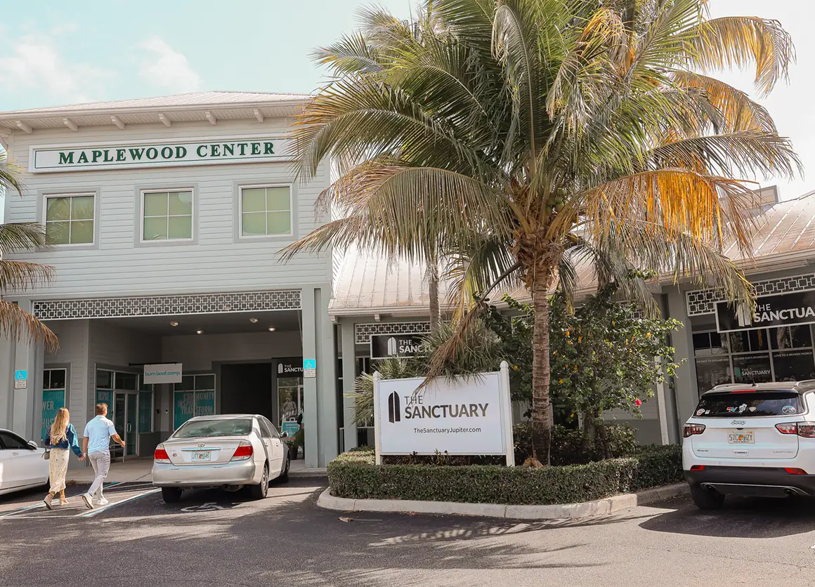 Exterior view of Maplewood Center with palm tree and sign for The Sanctuary in parking lot.