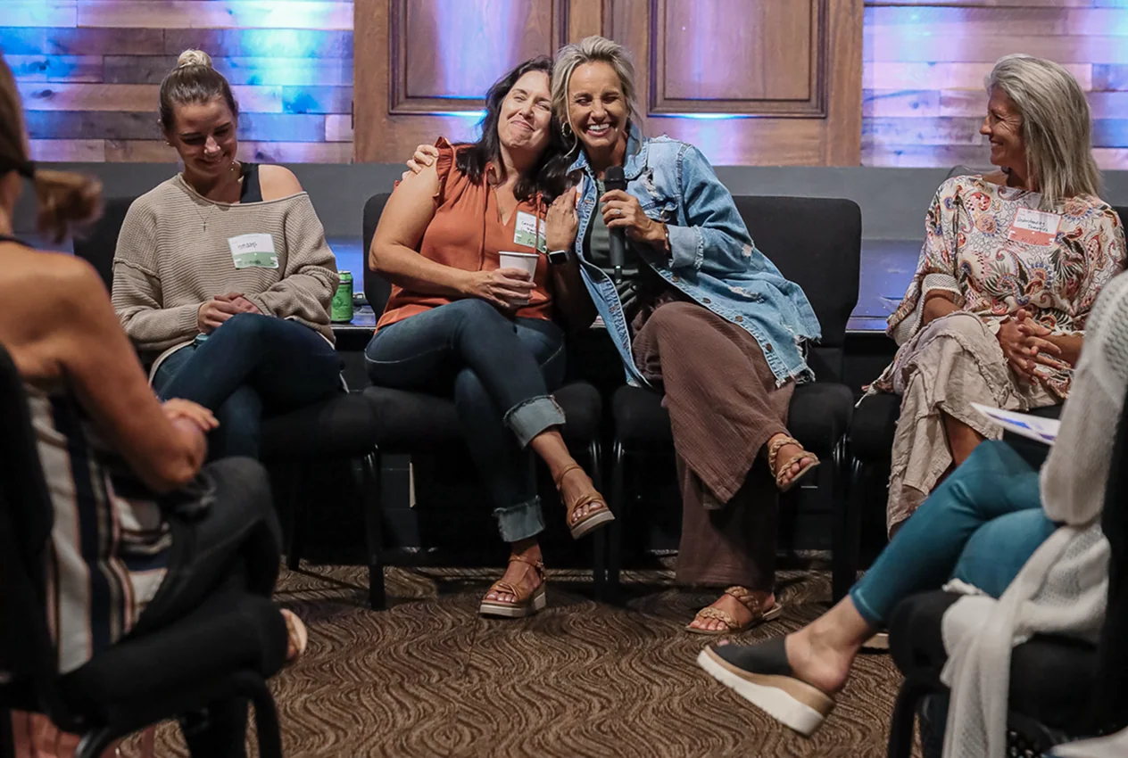 Group of women sitting in a circle engaged in a joyful discussion with one holding a microphone.