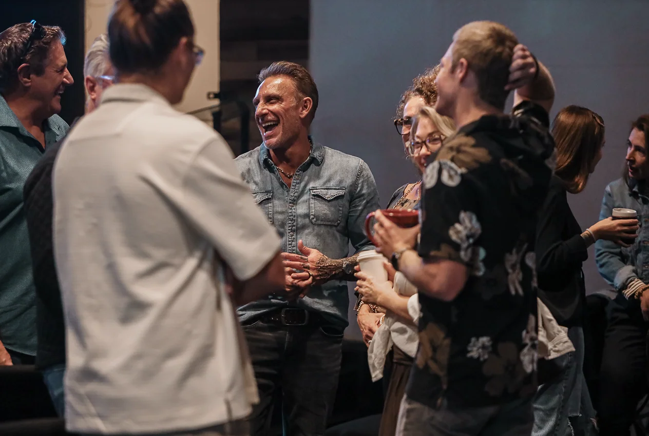 Group of diverse adults laughing and chatting while holding coffee cups indoors.