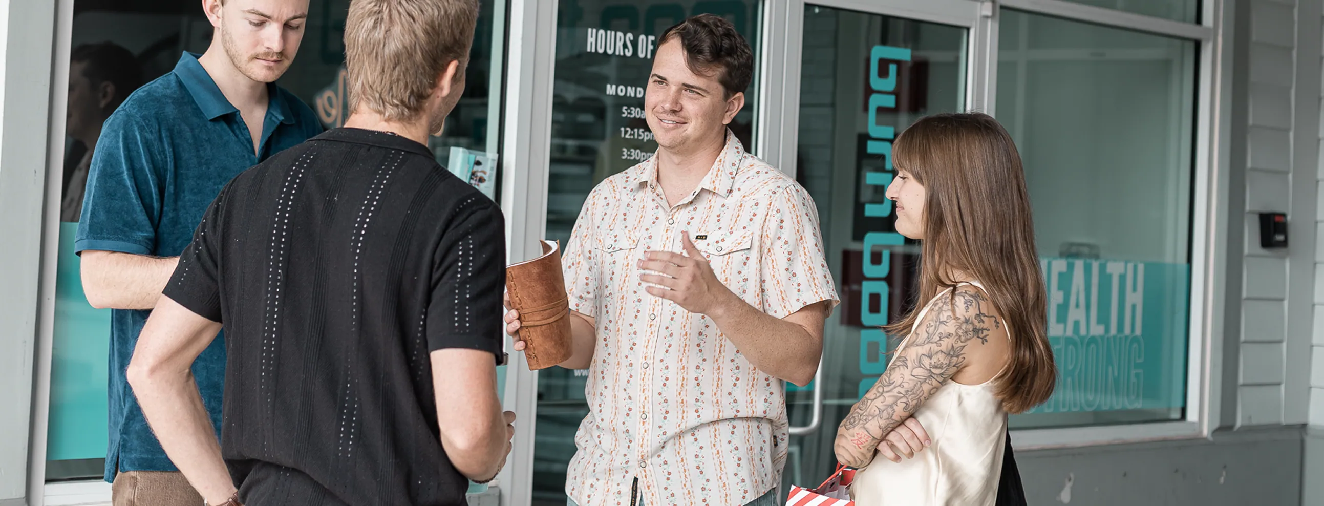 Four people standing outside a store having a conversation, one holding a brown notebook.