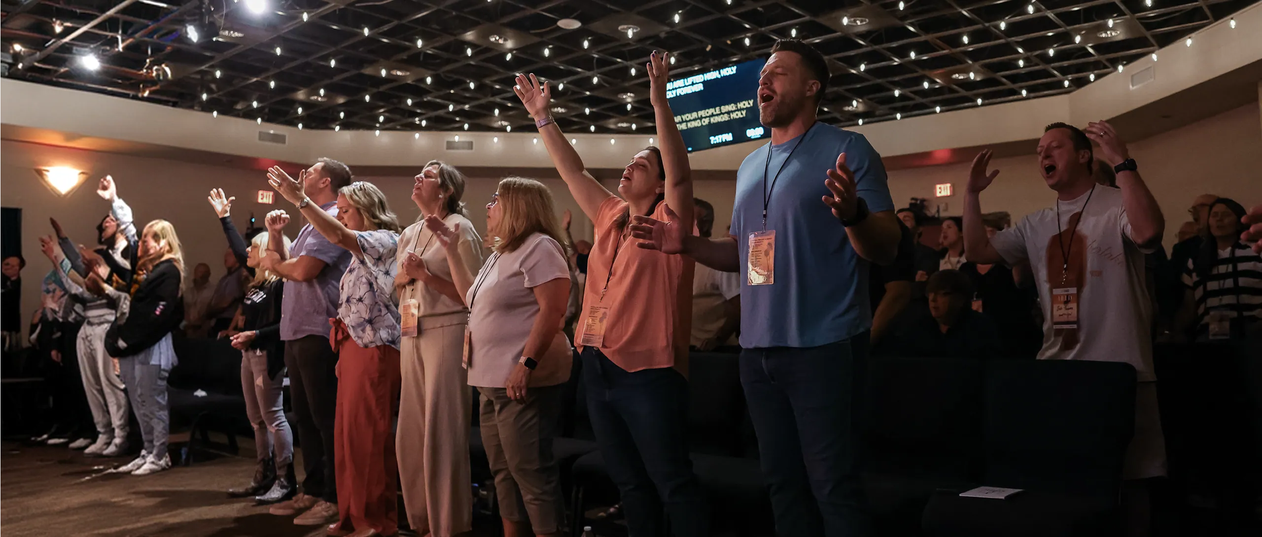 People standing in a church worshiping with hands raised and eyes closed during a service.