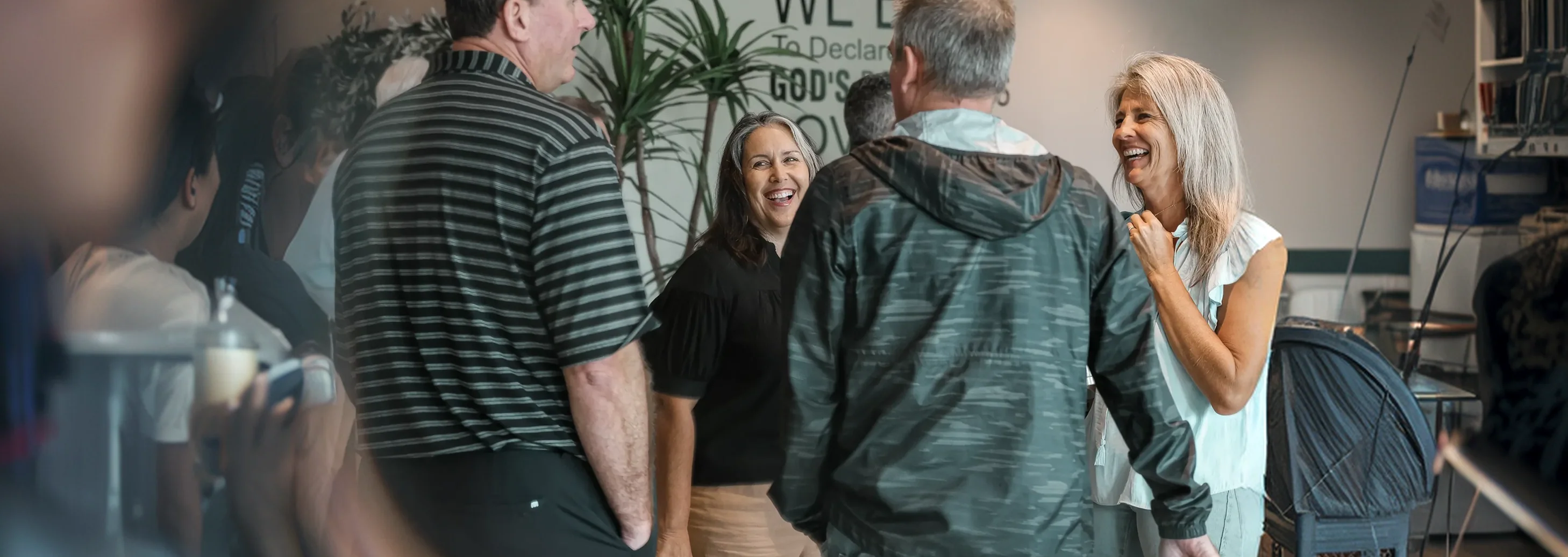 Group of adults laughing and chatting indoors in a casual social setting.