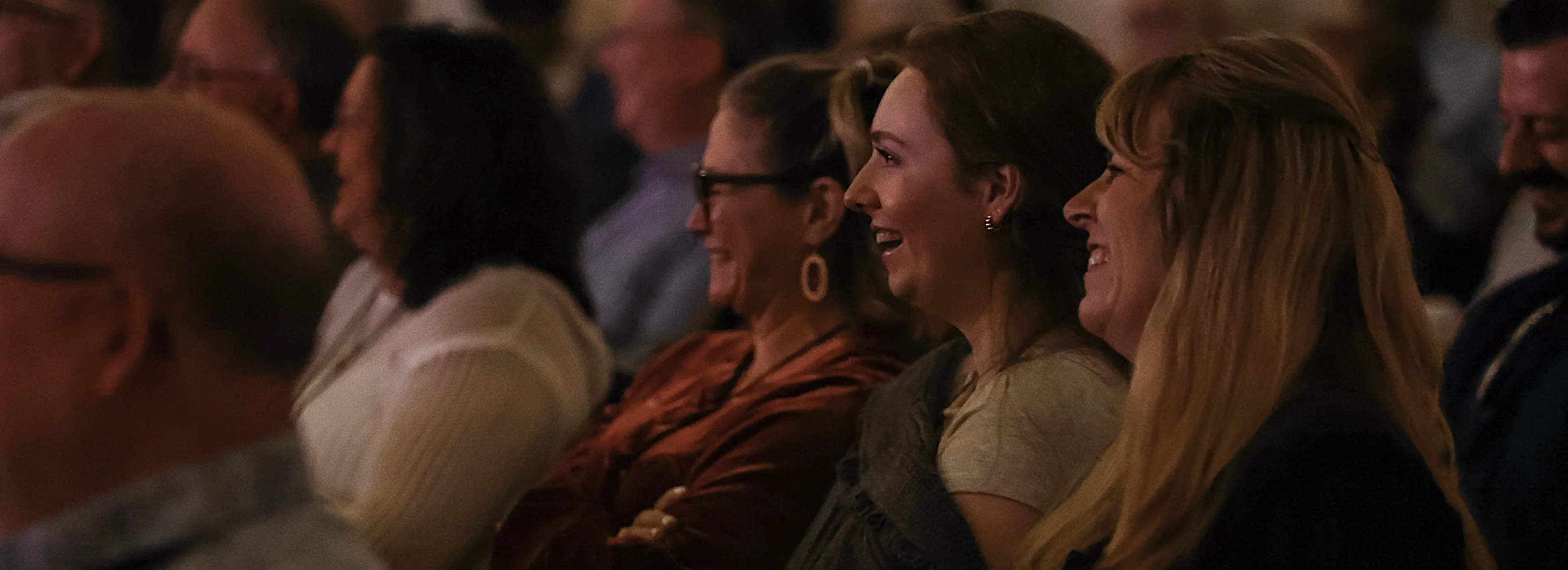 Audience seated in rows, smiling and laughing during an event or performance.