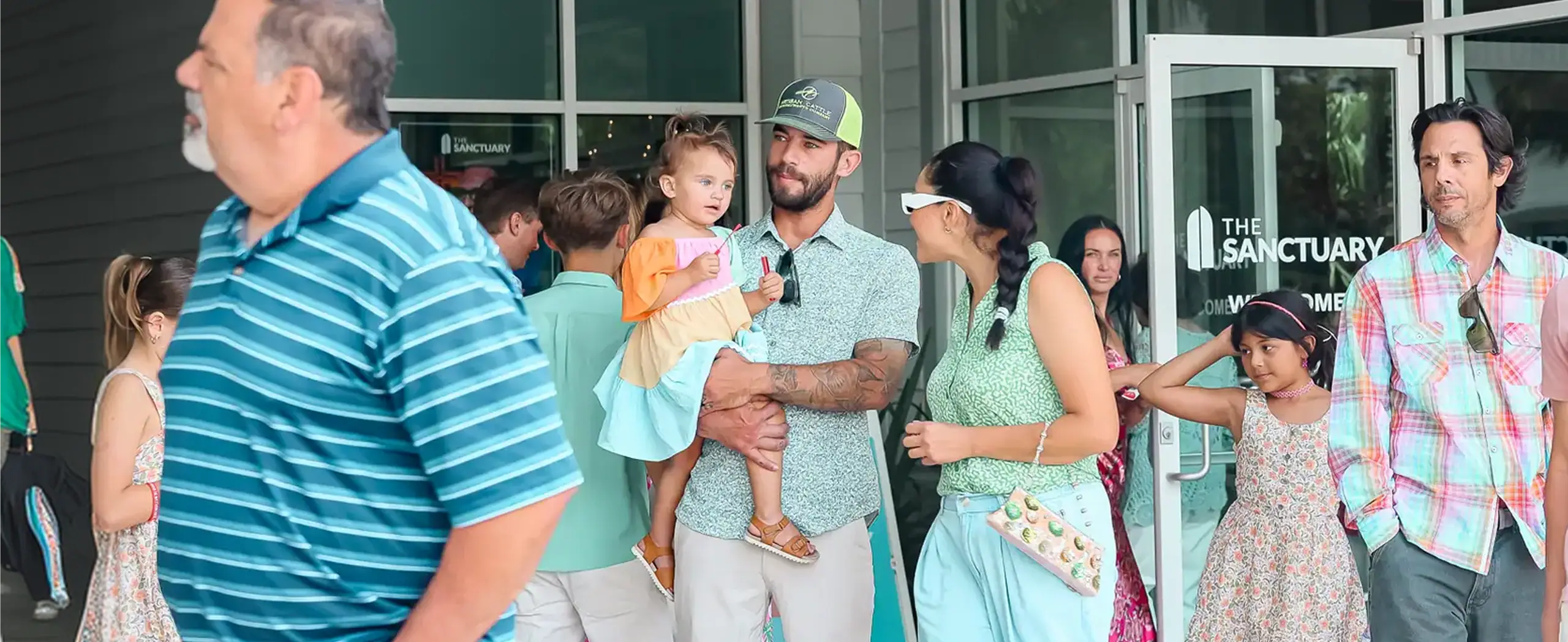 Diverse group of people, including a man holding a child, exiting a building labeled The Sanctuary.
