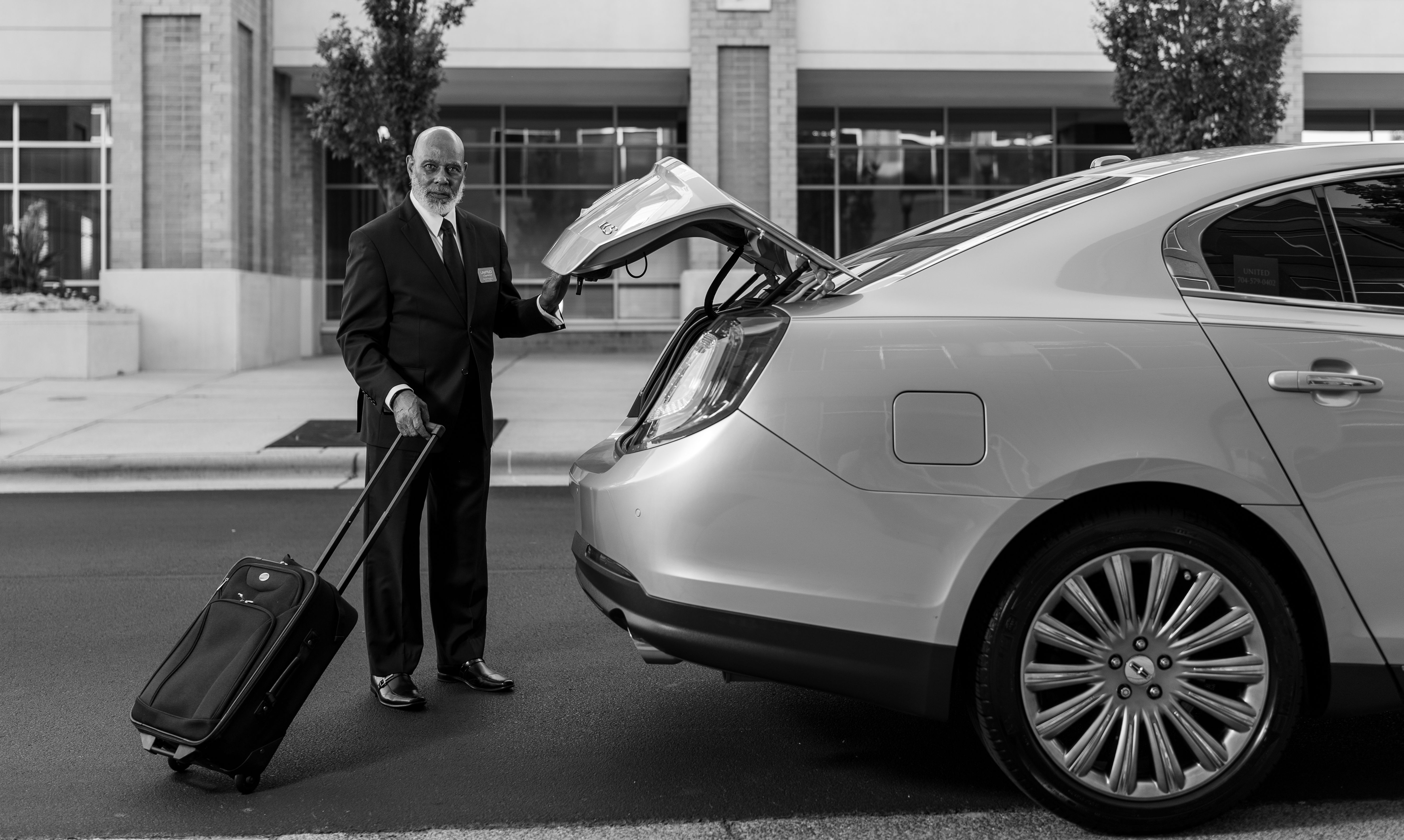 Professional chauffeur welcoming a traveller beside a luxury vehicle