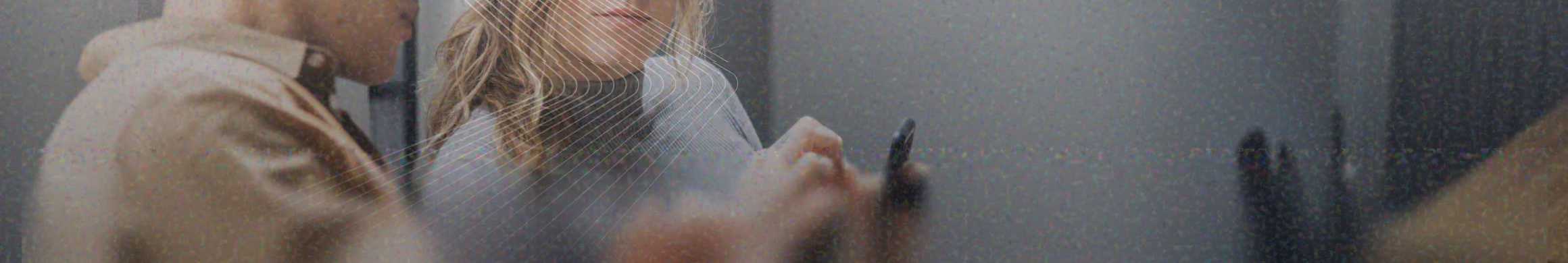 Two blurred individuals behind a glass wall with circular pattern, one person smiling and writing with a marker.