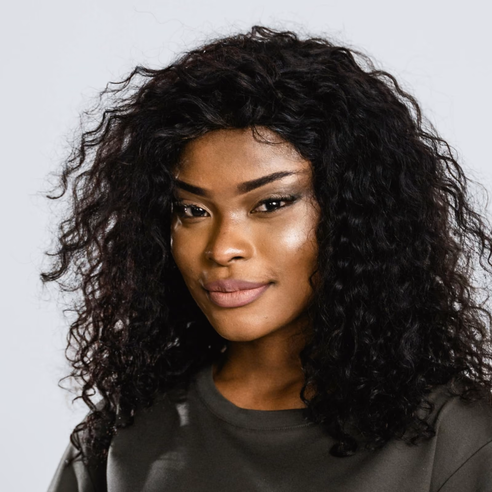 Portrait of a woman with curly black hair wearing a dark top against a plain background.
